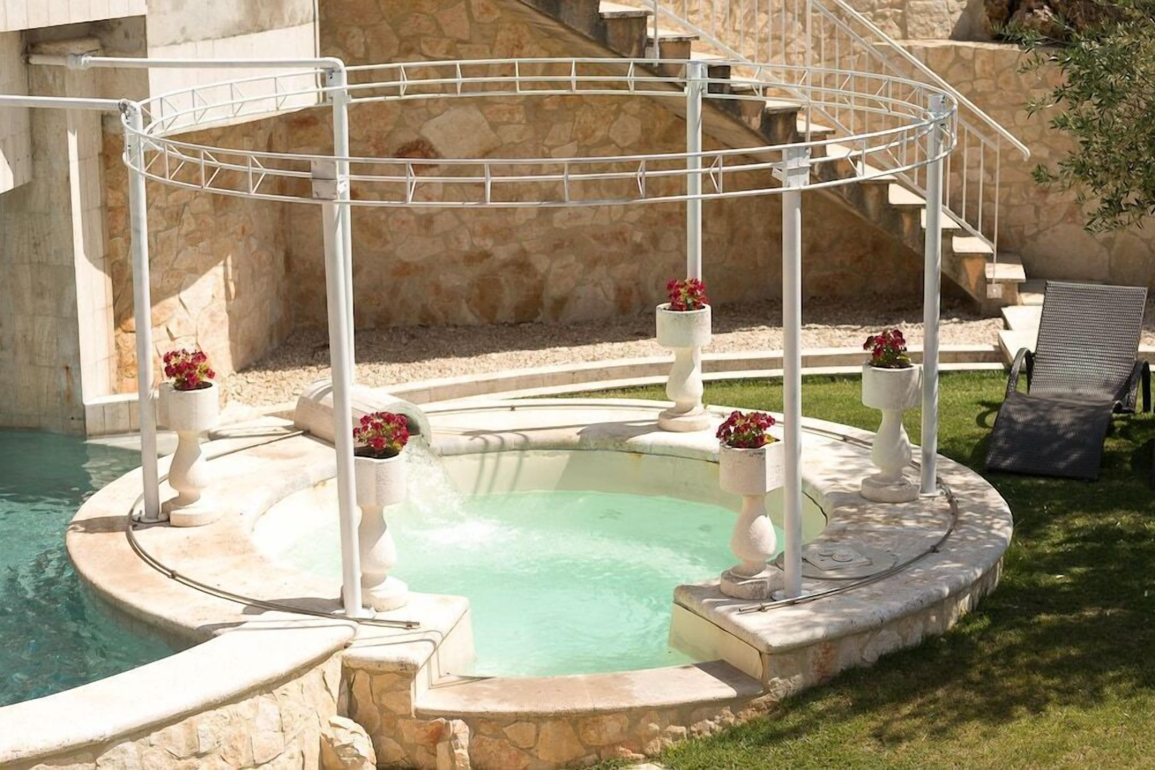 A circular pool with a central water feature, surrounded by stone steps and white balustrades.