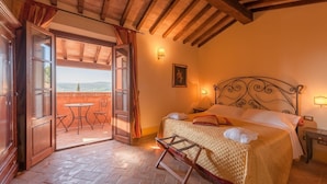 A bedroom with a bed, a nightstand, a wall-mounted lamp, and a view of the outdoors through an open door.