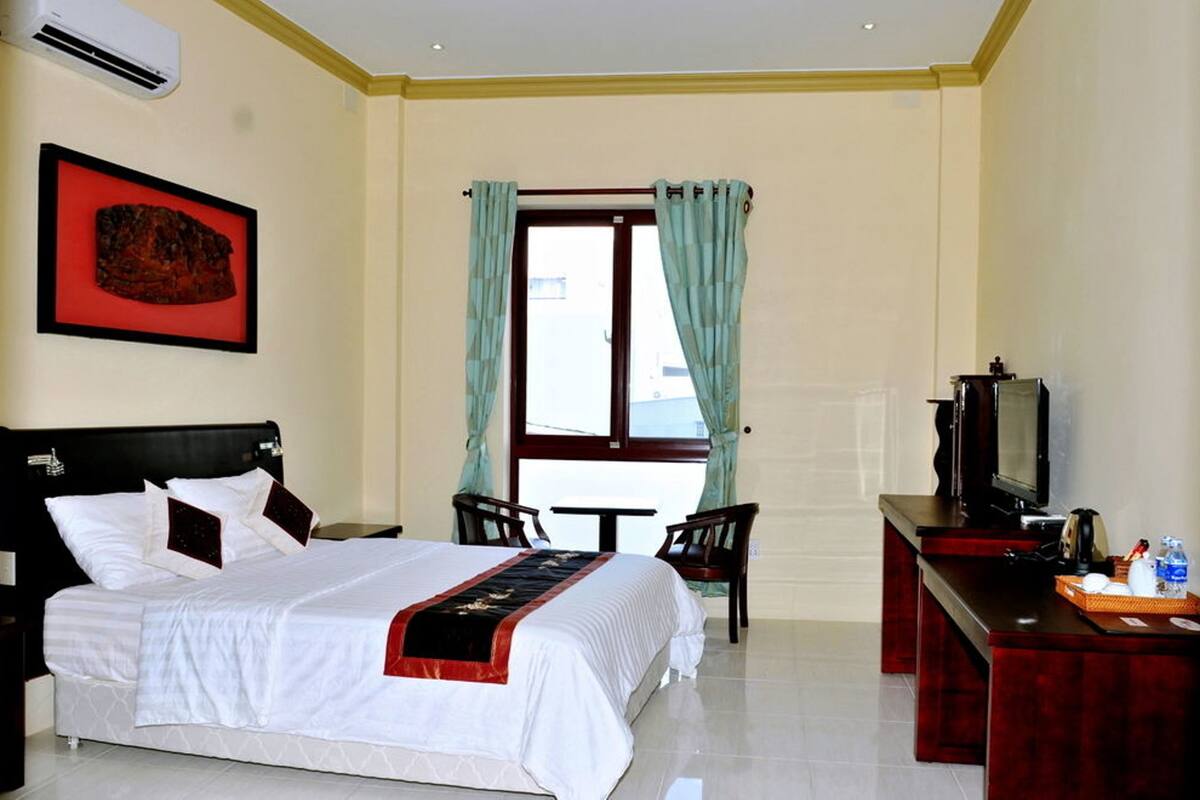 Una habitación de hotel con una cama, un escritorio con televisor, una mesita y una ventana con cortinas.