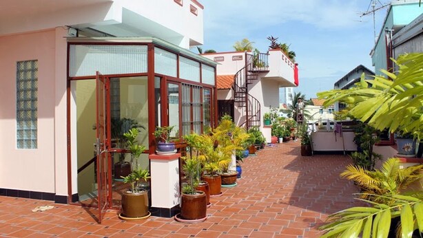 A courtyard with potted plants, a tiled floor, and a building with a glass door and windows. - Murray Guesthouse (Chau Doc)