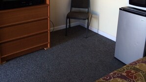 A room with a wooden TV stand, a small chair, a microwave, and a bed with patterned bedding. - Colonial Motel (Gallup)