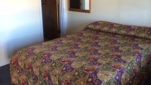 A bedroom with a patterned bedspread, a door, and a mirror on the wall. - Colonial Motel (Gallup)