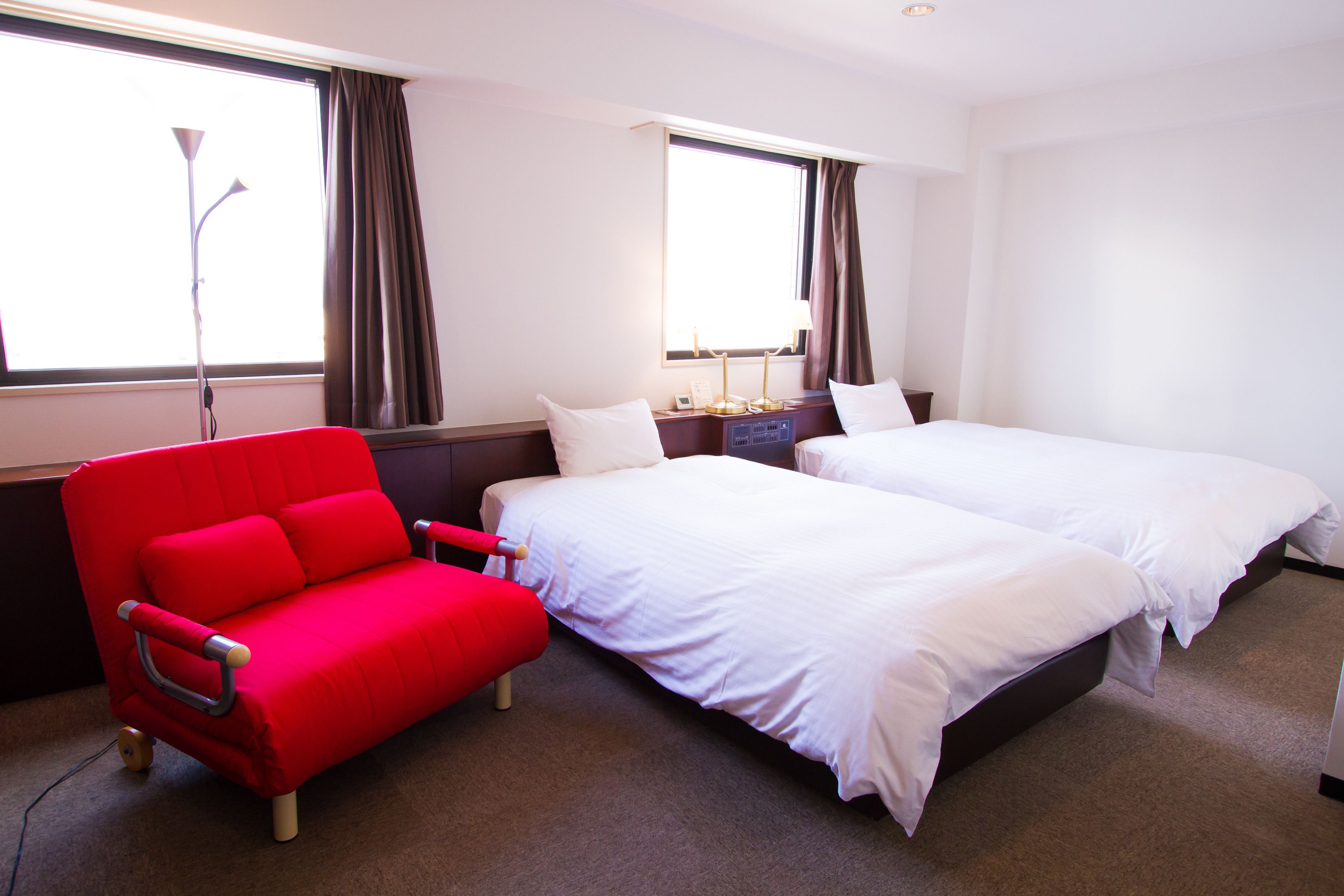 Una habitación de hotel con dos camas, un sofá rojo y una lámpara.