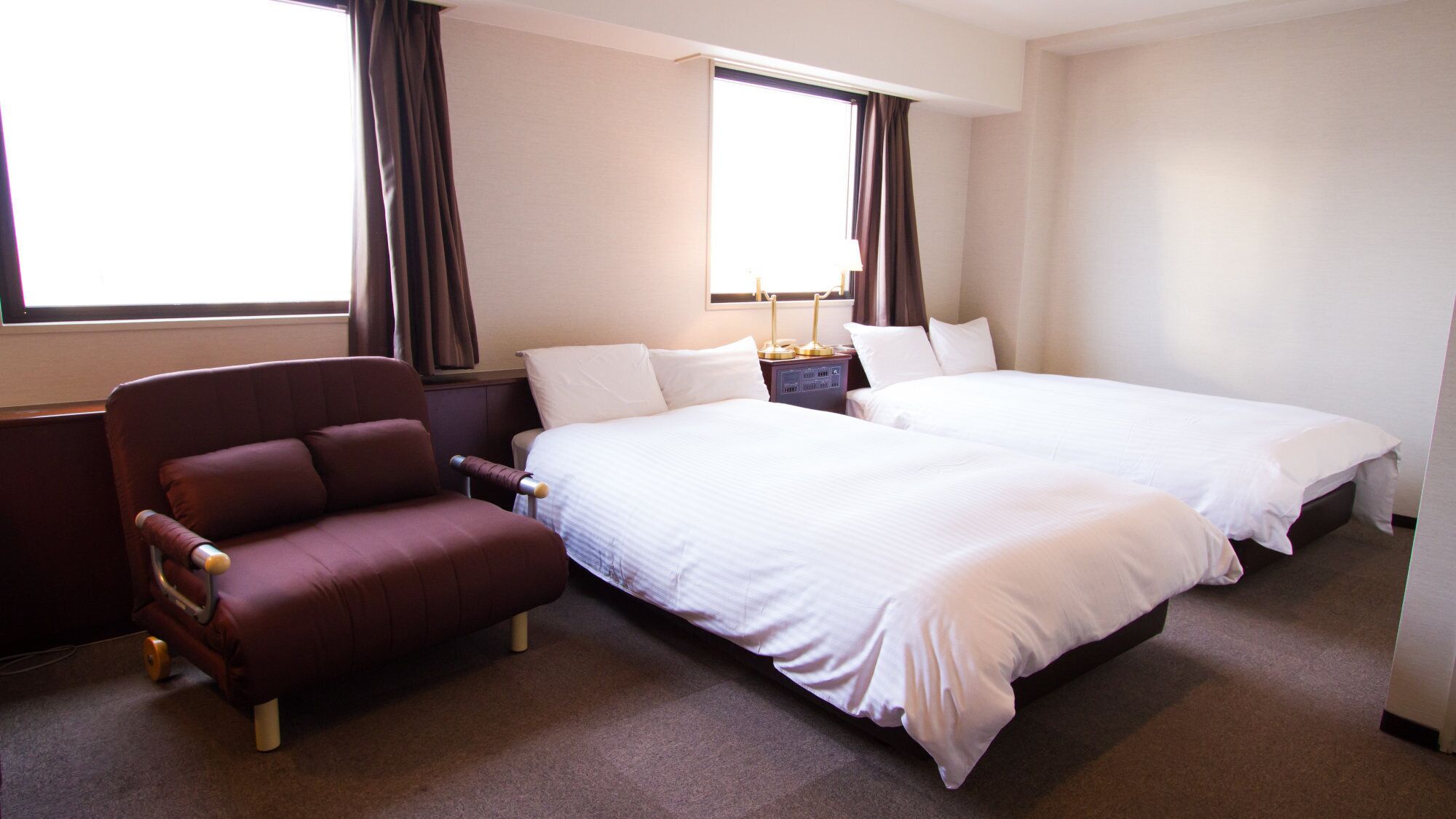 Een hotelkamer met twee bedden, een stoel, een nachtkastje en een raam met gordijnen.