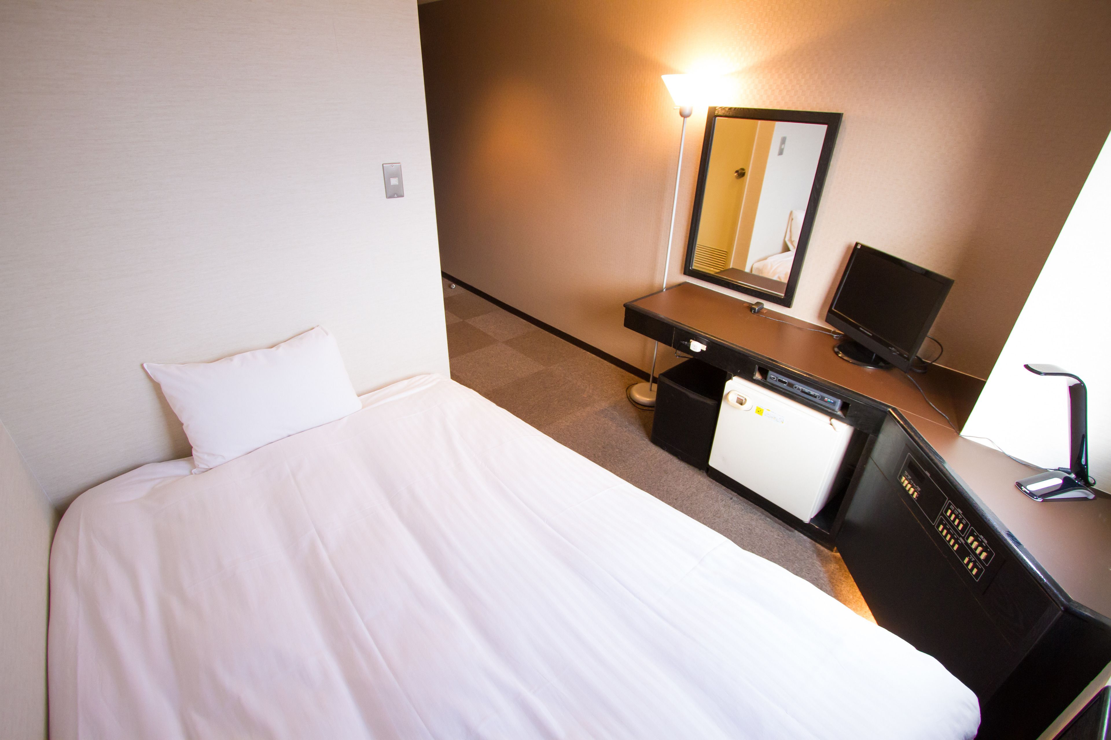Et hotelværelse med en seng, et skrivebord med computer, et spejl og en lampe.