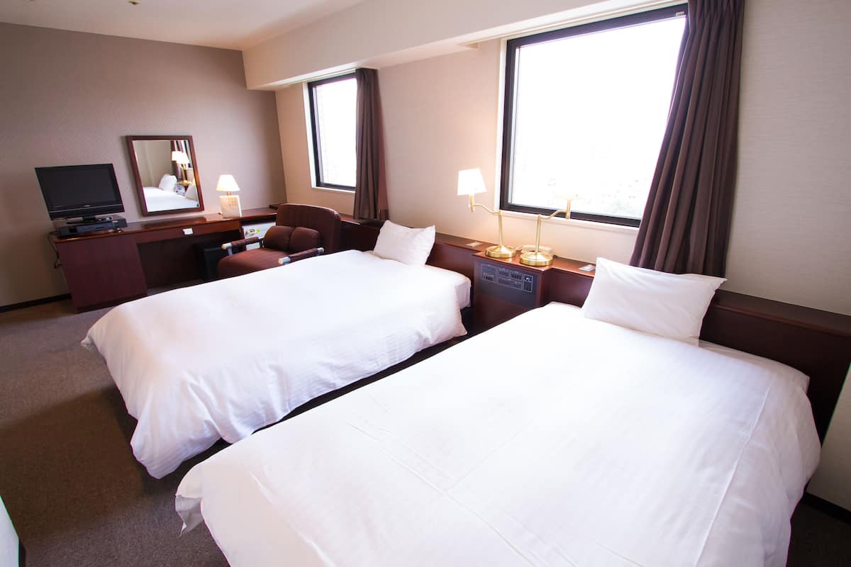 Une chambre d’hôtel avec deux lits, un bureau avec une télévision, une chaise et une lampe.