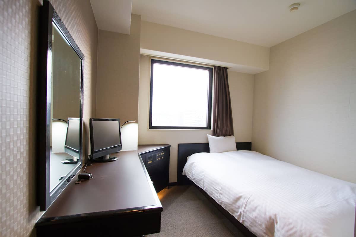 Une chambre d’hôtel avec un lit, un bureau avec un ordinateur, une télévision et une fenêtre avec des rideaux.