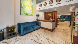 A hotel lobby with a blue sofa, a large floral painting, clocks displaying times in New York, Paris, Hanoi, Beijing, and Tokyo, and a reception desk. - Midori Boutique Hotel (Hanoi)