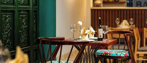 Un comedor con mesas y sillas de madera, una botella de vino y un florero con una flor.
