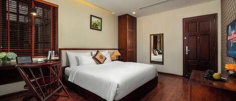 A hotel room with a large bed, wooden floor, a desk with a laptop, a chair, a TV, and a door.