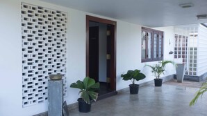 Um corredor com parede branca, porta de madeira e plantas em vasos.
