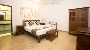 Quarto com cama, cabeceira de madeira, mesas de cabeceira, um criado-mudo, guarda-roupa e ventilador de teto.