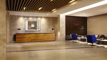 Un hall d’entrée moderne avec un comptoir d’accueil en bois, des chaises bleues et un grand tableau encadré au mur.