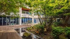 A modern building with a glass facade, outdoor seating area, and a small water feature. - The Annex (Seogwipo)