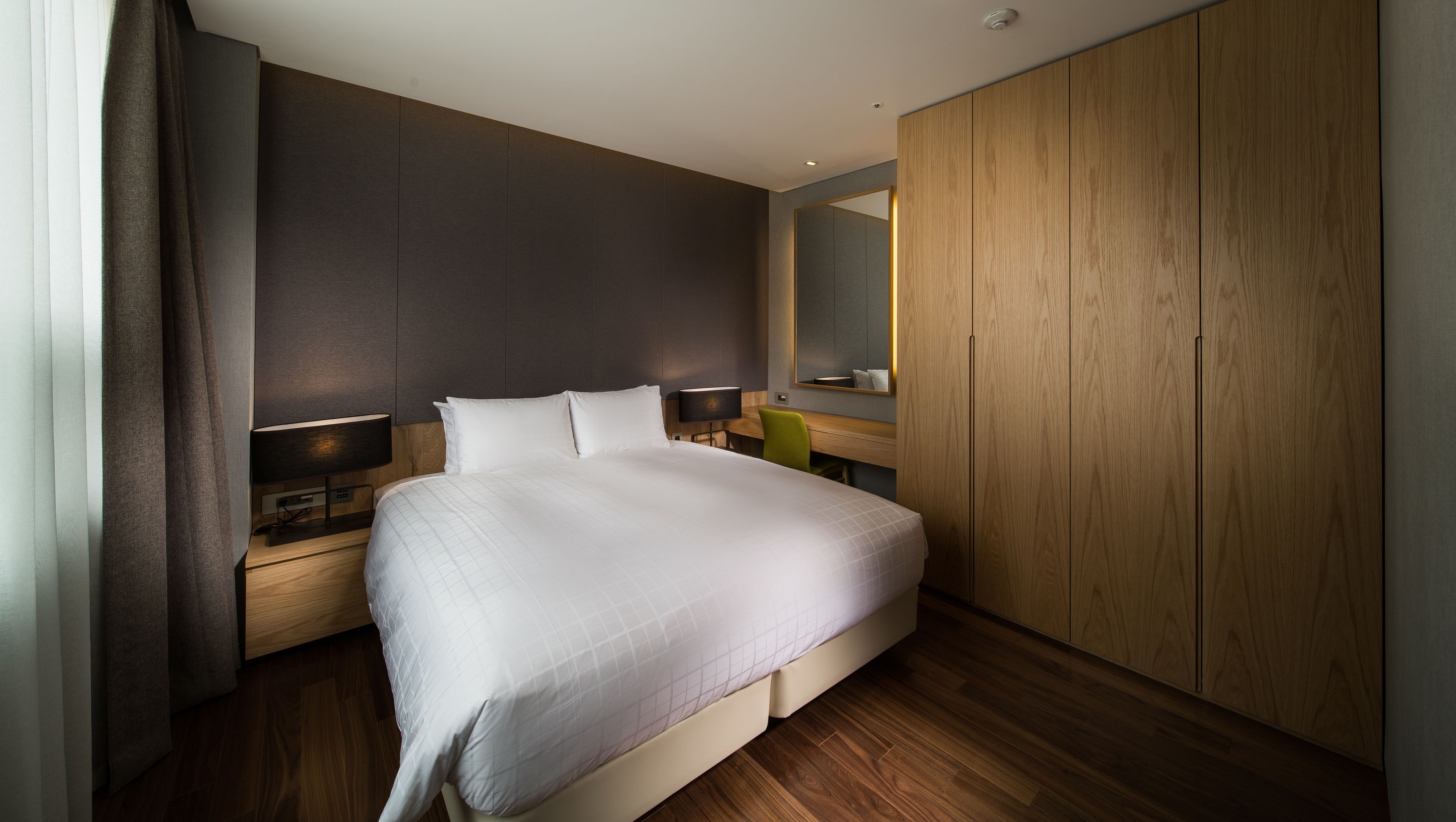 Une chambre d’hôtel moderne avec un grand lit, une armoire en bois et un bureau avec une chaise.