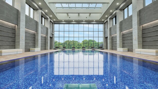 An indoor swimming pool with clear glass walls, a tiled floor, and a view of trees outside. - The Annex (Seogwipo)