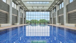 Una piscina interior con paredes de vidrio transparente, suelo de baldosas y vistas a árboles fuera.