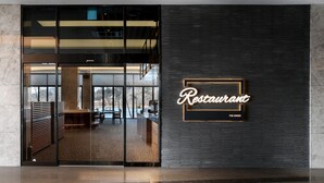 A modern restaurant with a glass entrance, a wooden reception desk, and a sign that reads "Restaurant The Annex". - The Annex (Seogwipo)