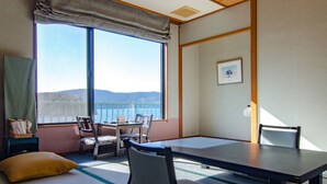 A traditional Japanese-style room with tatami flooring, a low table, and chairs. A large window offers a view of the sea and hills. - Hotel Musashiya (Hakone)