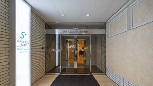 Entrada de hotel con puerta de cristal, un letrero y suelo de baldosas.