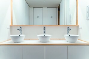 Une salle de bain moderne avec trois lavabos blancs, chacun doté d’un robinet distinct, et un grand miroir au-dessus des lavabos.