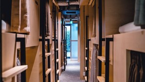 A narrow hallway with wooden shelving units on either side, leading to a bright exit. - UNPLAN Kagurazaka - Hostel (Tokyo)