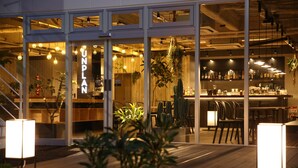 A modern bar with a wooden interior, glass doors, and hanging plants. - UNPLAN Kagurazaka - Hostel (Tokyo)