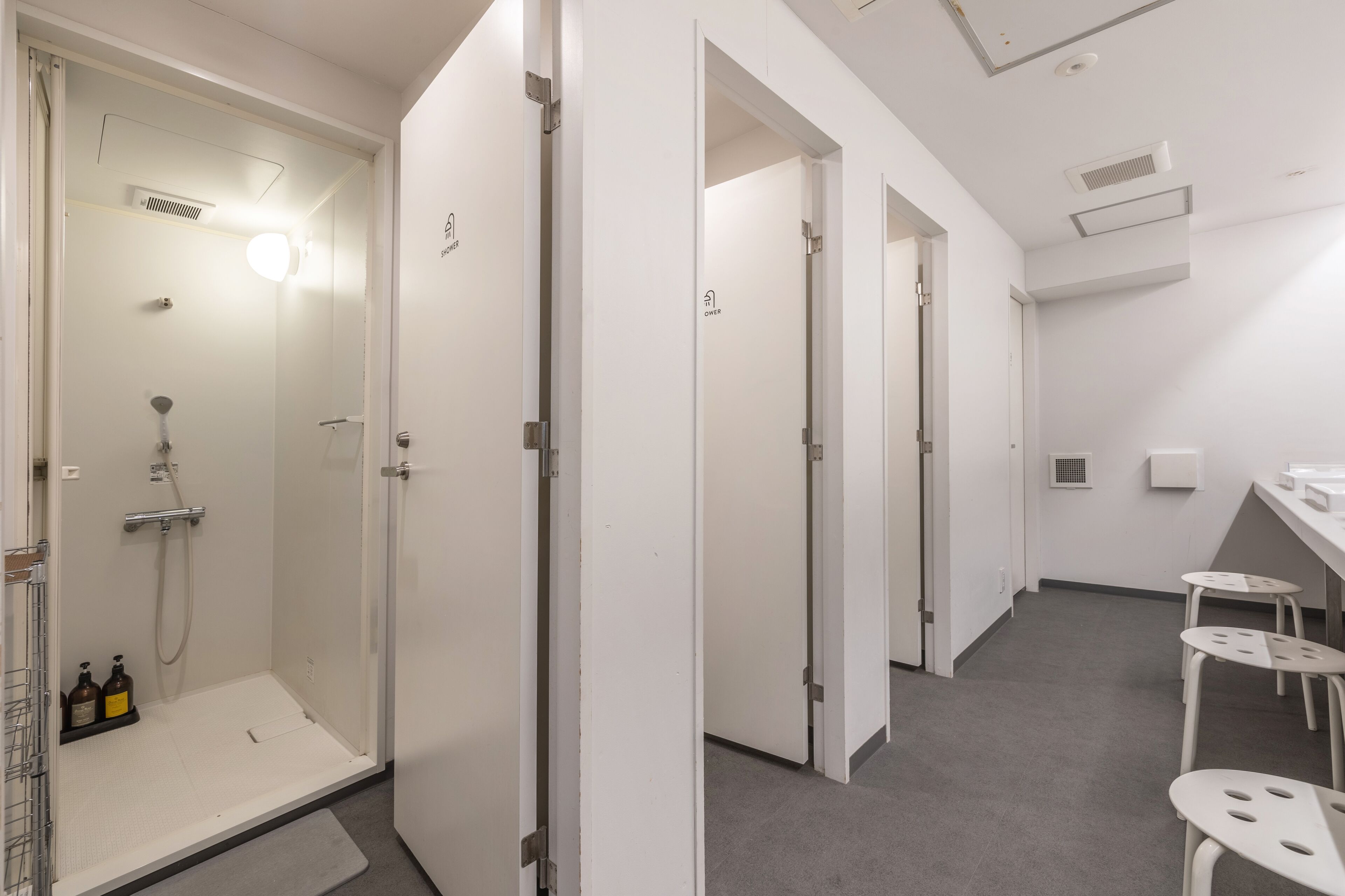 A modern bathroom with a glass-enclosed shower, a vanity with a mirror, and a small seating area with stools.
