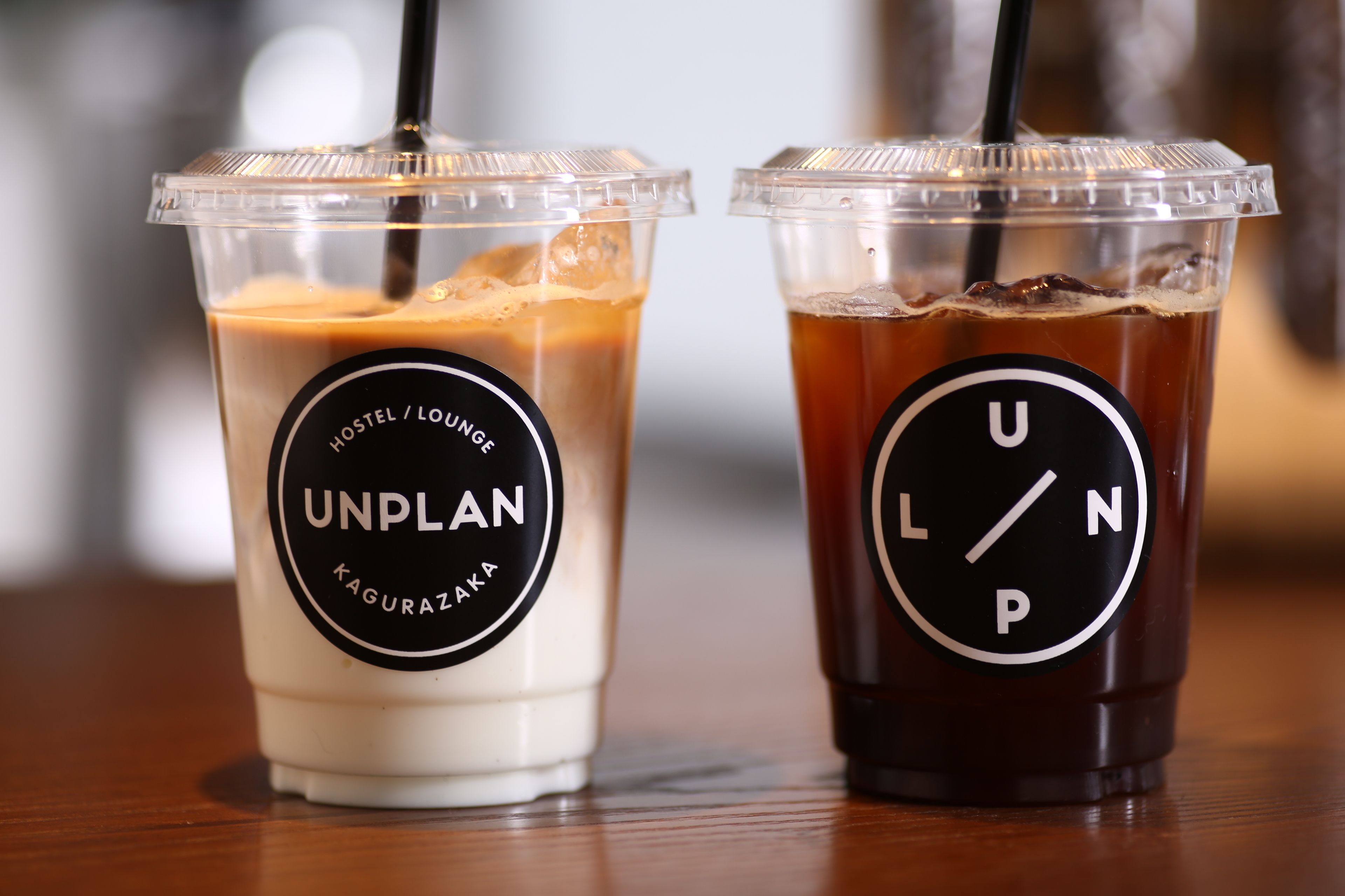 Two plastic cups with black lids and straws, one labeled "UNPLAN" and the other "UNPLAN".