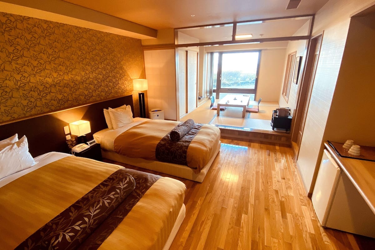 A hotel room with two beds, a desk, a chair, a TV, and a window with a view.