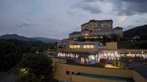 Un hotel de varios pisos, un patio con fuentes de agua y montañas al fondo.