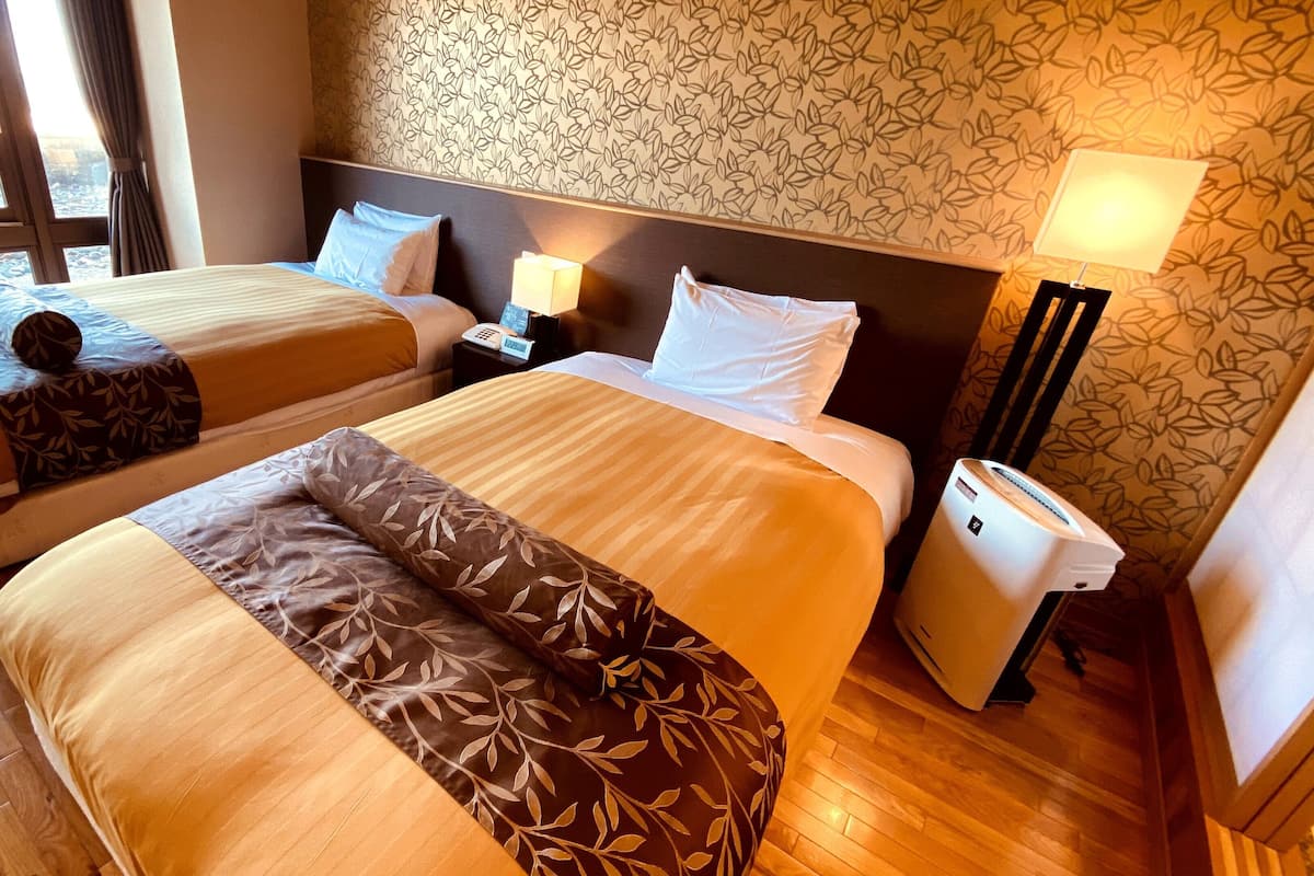 A hotel room with two beds, a nightstand with a lamp, a telephone, and a wall with a leaf pattern.