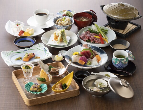 A variety of dishes and drinks arranged on a table, including sushi, sashimi, and a teapot.