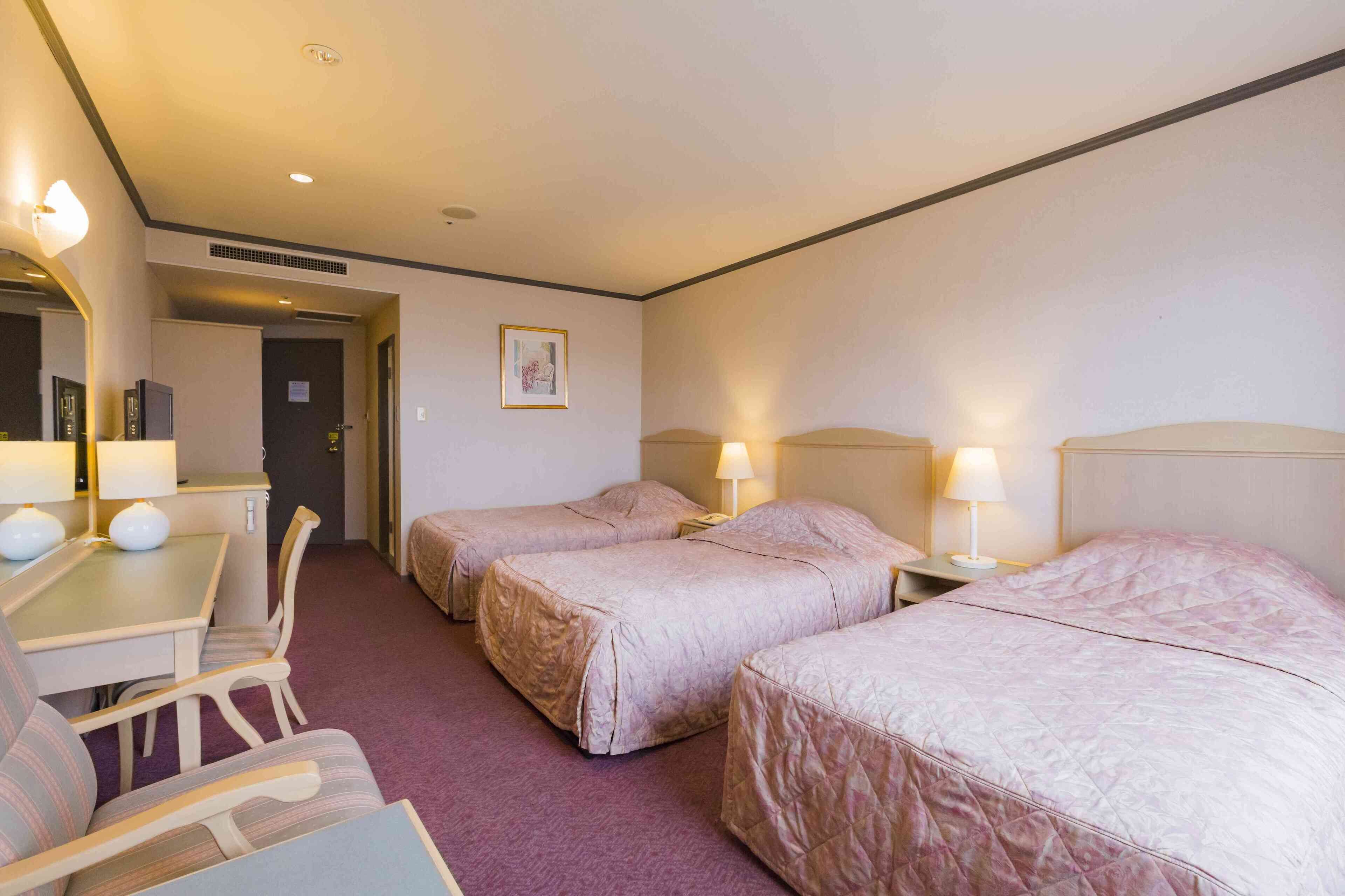 Une chambre d’hôtel avec deux lits, un bureau et une chaise. Il y a deux lampes de chevet et un tableau au mur.