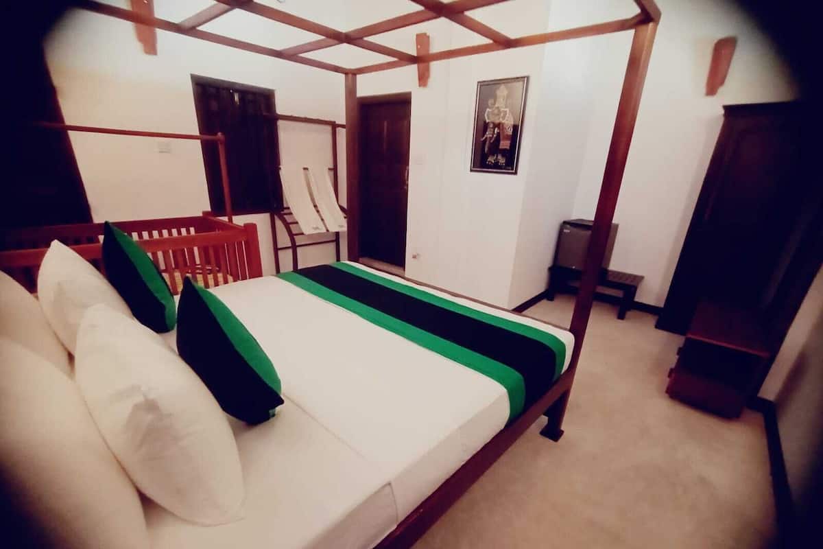 Une pièce avec un lit, une chaise en bois, une porte et une affiche accrochée au mur.