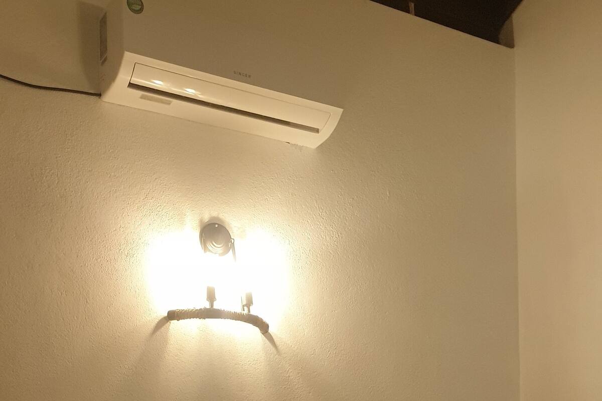 Une chambre d’hôtel comprenant un lit, une table de chevet, un climatiseur fixé au mur et un luminaire fixé au mur.