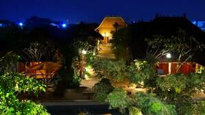 A traditional building with a thatched roof, surrounded by lush greenery and illuminated by warm lighting.