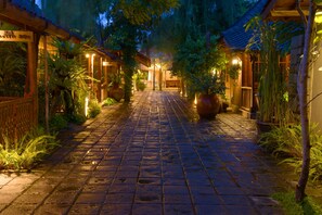 A paved pathway leading to a building with traditional architecture, surrounded by lush greenery and illuminated by warm lighting. - WARISAN Heritage Boutique Hotel (Baki)