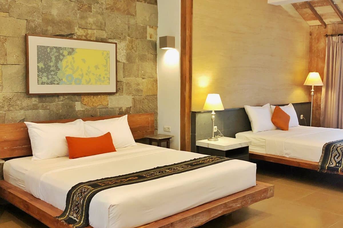A hotel room with two beds, a stone wall, a framed artwork, and a patterned rug.