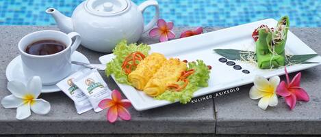 A table with a white teapot, a cup of tea, a plate of food, and some flowers by a pool.
