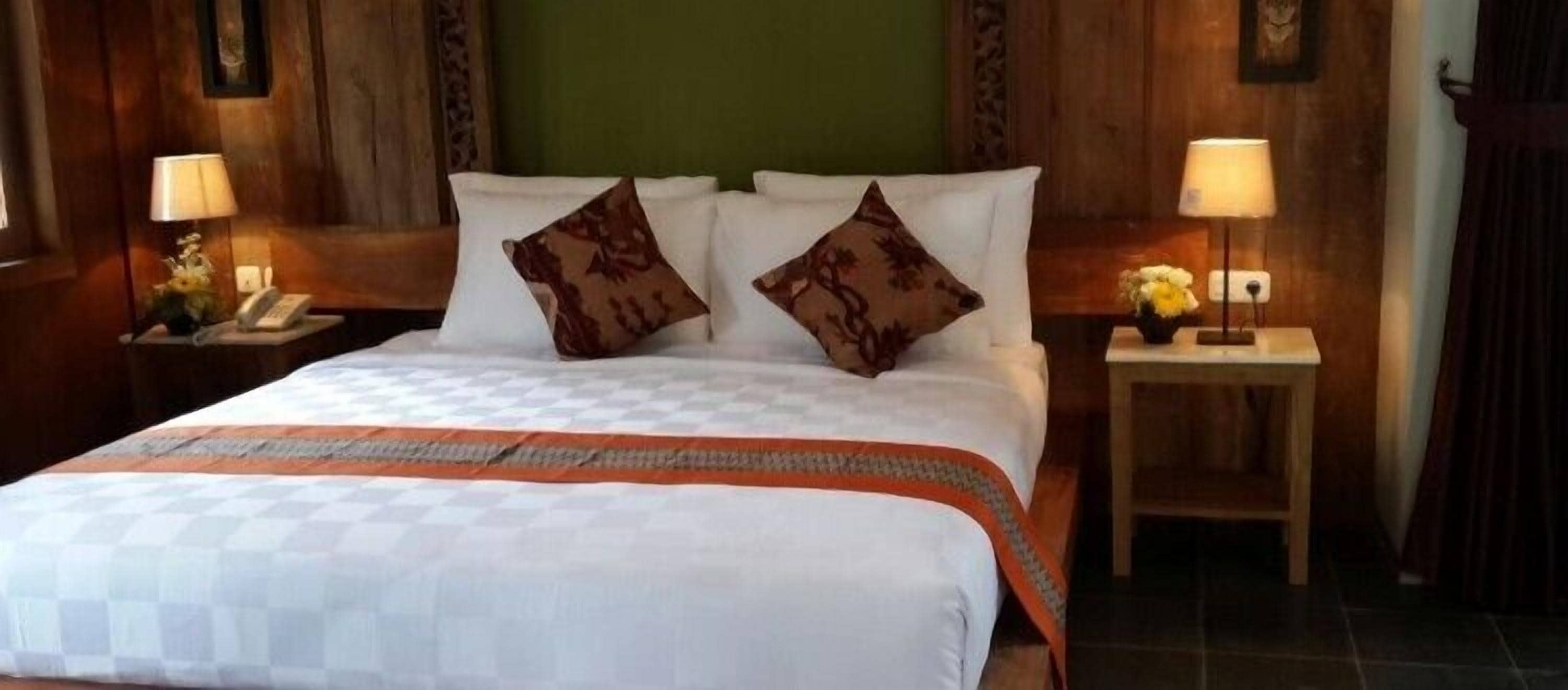 A neatly made bed with a checkered bedspread and two decorative pillows, flanked by bedside tables with lamps and floral arrangements.