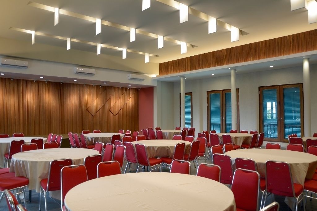 A conference room with multiple round tables and red chairs, equipped with ceiling lights and large windows.
