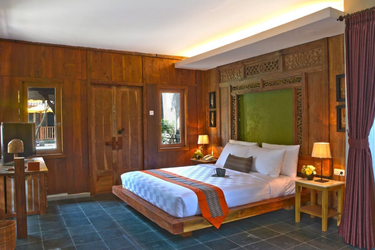 A wooden room with a bed, two bedside tables, a desk, and a window.