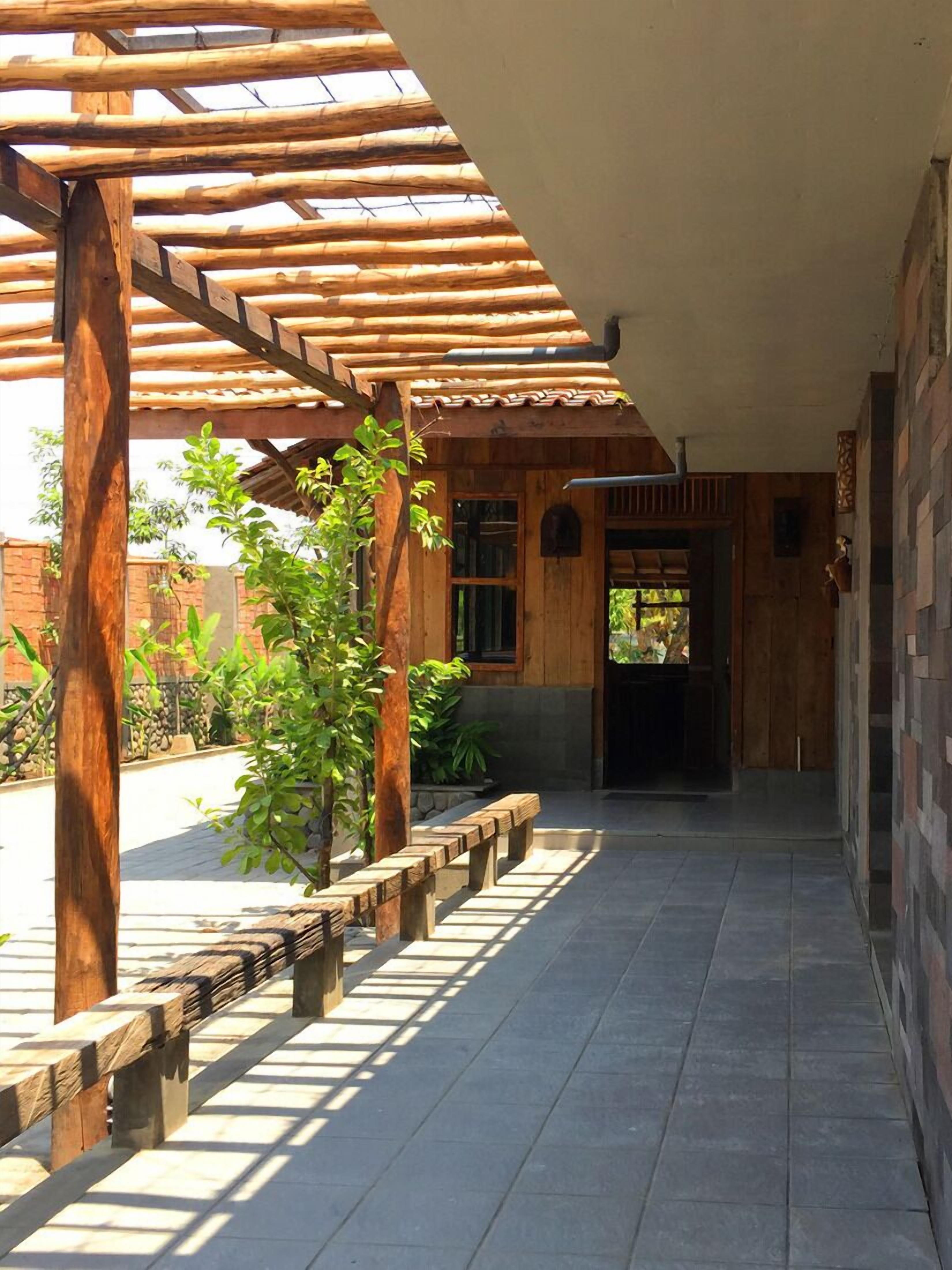 A covered outdoor area with wooden beams and a tiled floor, leading to a building entrance.