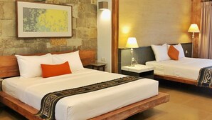 A hotel room with two beds, a stone wall, a framed picture, and a patterned rug.
