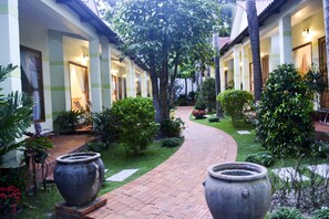 A courtyard with a brick pathway, potted plants, and a large tree. - Ngoc Viet Bungalow (Phu Quoc)