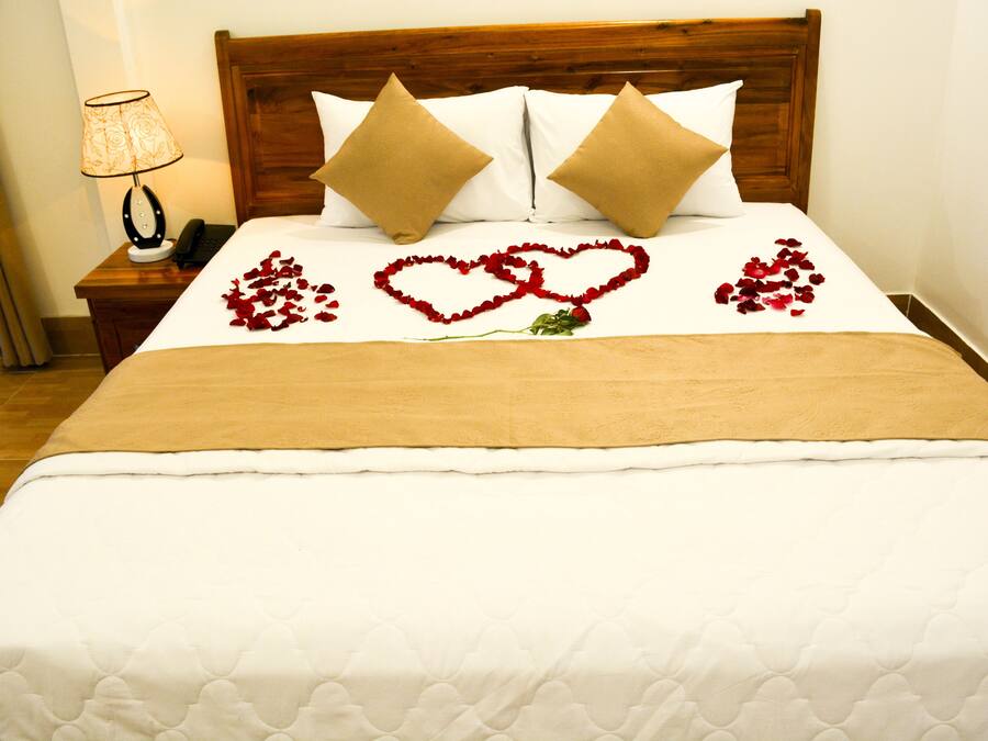 Cama bem arrumada com colcha branca, duas almofadas bege e cabeceira de madeira.