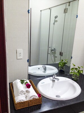 A bathroom with two sinks, a shower, and a mirror. There is a basket of towels and a potted plant on the counter.