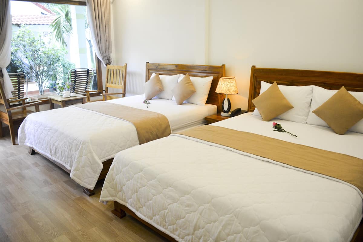 Two single beds with wooden headboards, a bedside table with a lamp, and a chair with a table.