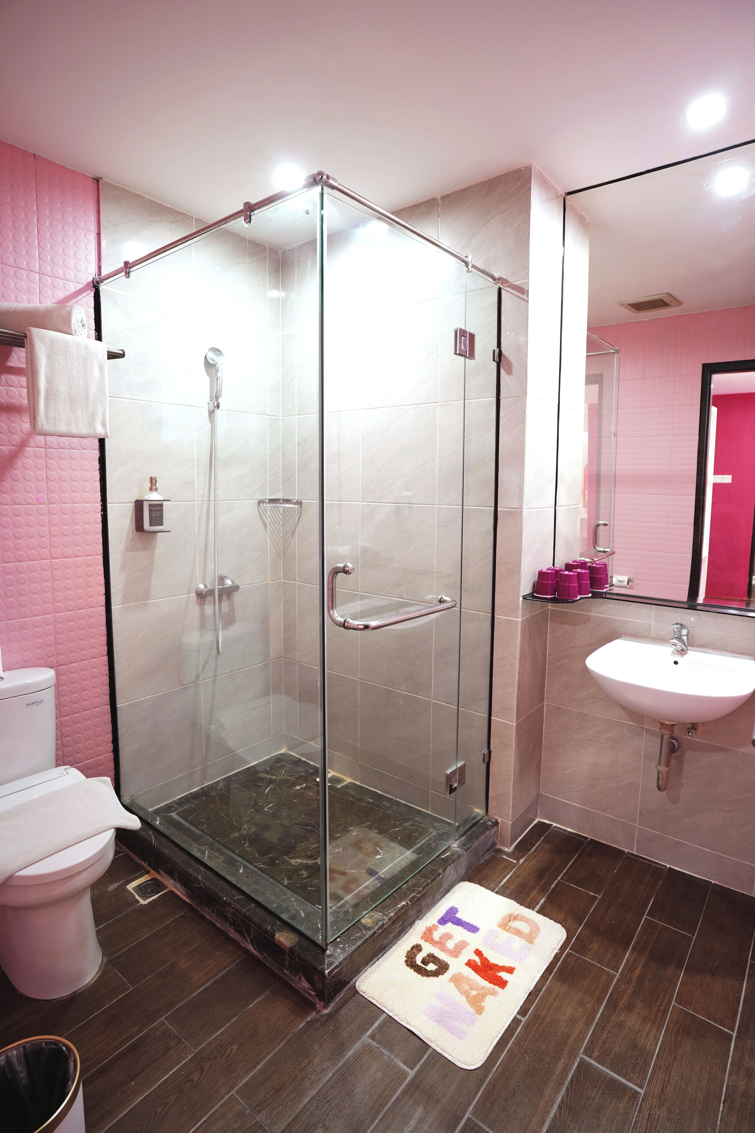 Un bagno con doccia vetrata, un lavandino bianco e una parete rivestita di piastrelle rosa.